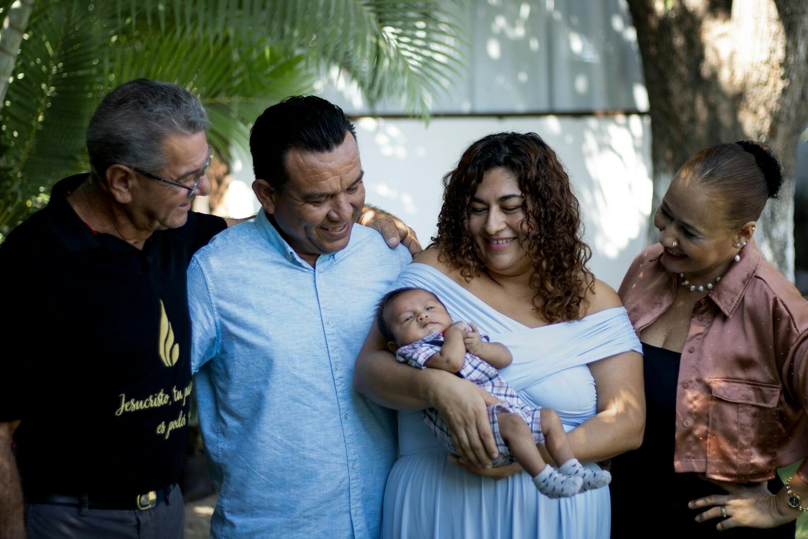 Joyful family gathering with proud parents and grandparents holding a newborn baby outdoors.