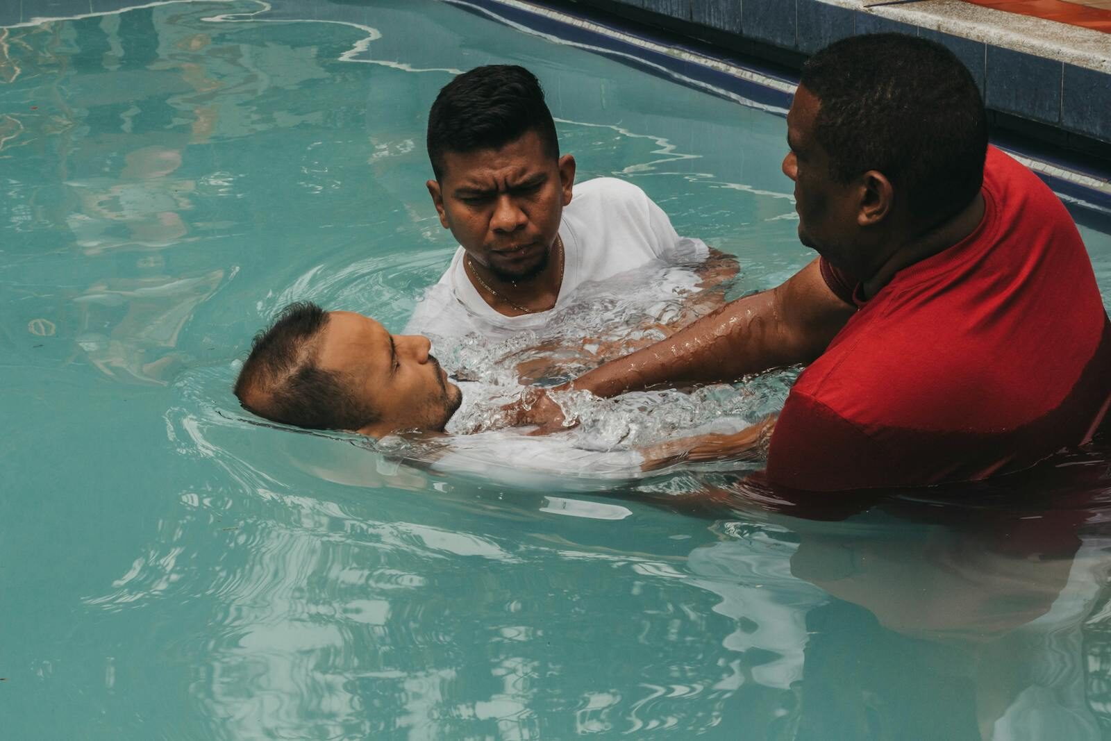 Three men performing a baptism in a swimming pool, symbolizing faith and tradition.